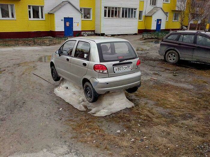 Small silver car stuck parked on melting snow patch in a residential area, illustrating funny and unusual parking fails.