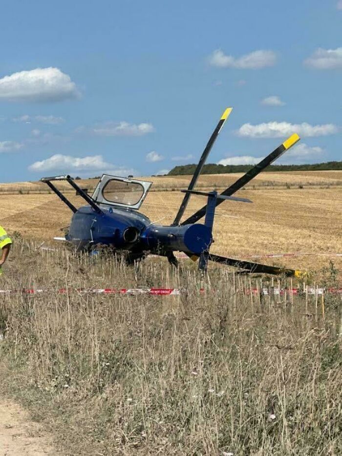 Blue helicopter crashed in a field surrounded by warning tape, illustrating extreme parking fails in an open rural area.