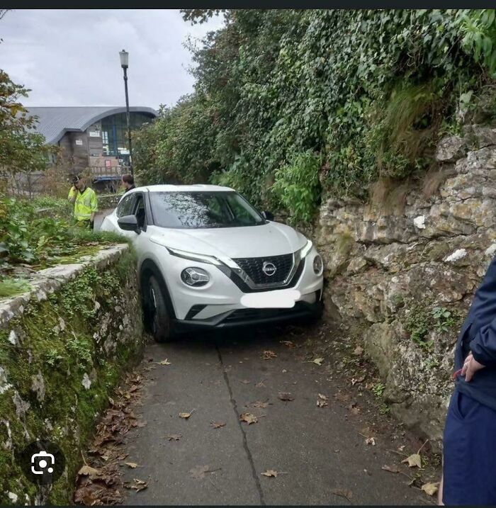 White Nissan car stuck in a narrow alley between stone walls, illustrating a parking fail on a tight path.
