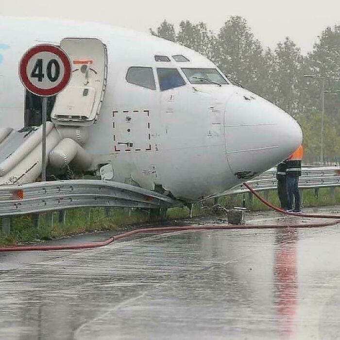 Front section of an airplane parked awkwardly behind a guardrail on a wet road, illustrating a notable parking fail.