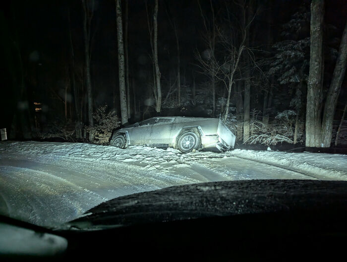 A poorly parked car covered in snow stuck off-road at night in a forest, illustrating parking fails shared online.