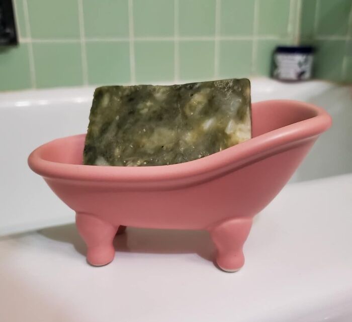 Small pink bathtub soap holder with a bar of green soap, a sneakily useful decor item for the bathroom sink area