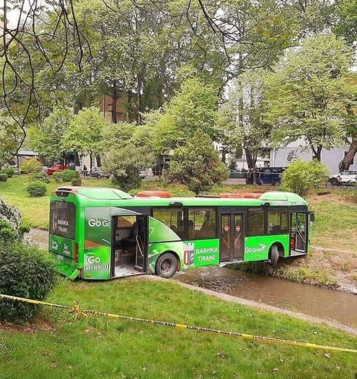 Green hybrid bus stuck in a small stream, demonstrating one of many parking fails shared online.