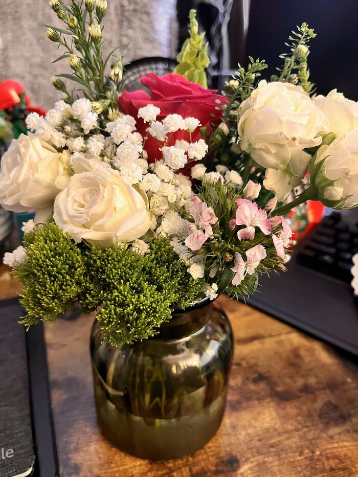 Bouquet of white and red roses with green foliage in a glass jar symbolizing wholesome kind neighbors' thoughtful gesture.