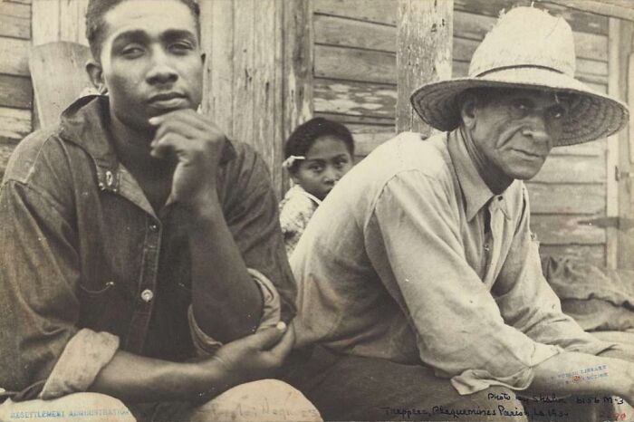 Two men and a child sitting outside a wooden building during the Great Depression, capturing the era's hardship.
