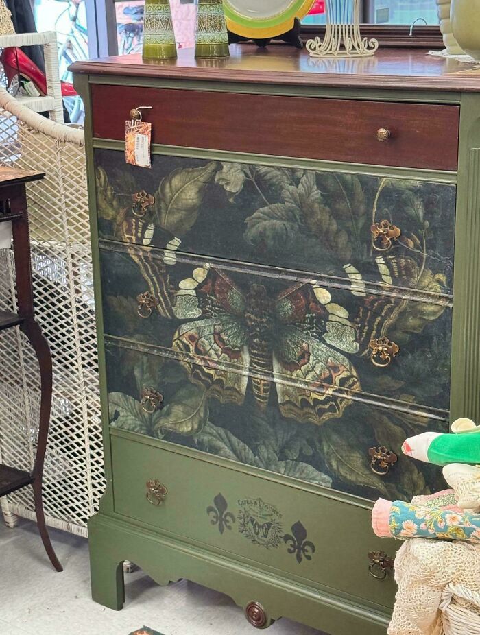 Vintage painted thrift store dresser with butterfly design and floral details in a cozy secondhand shop setting
