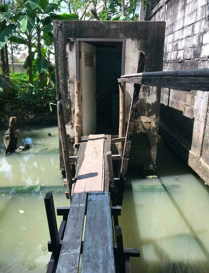Narrow, unstable wooden bridge leading to a dark, open door in a concrete structure over murky water, creating a creepy moment.