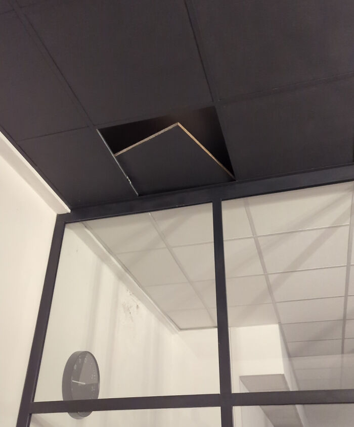 Office ceiling with a displaced black panel above a glass partition, creating a creepy and unsettling moment captured indoors.