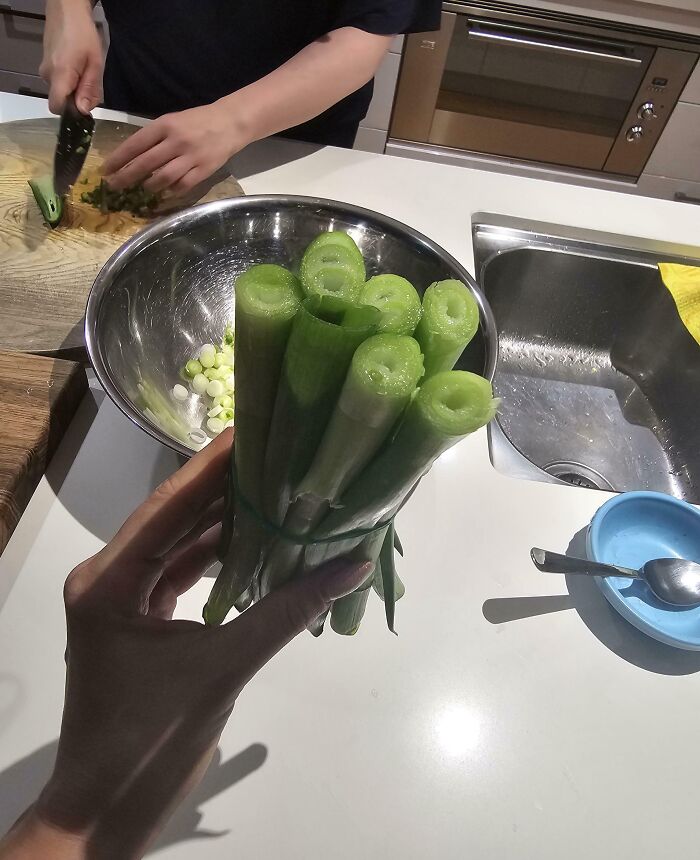 Mano sosteniendo cebollines frescos mientras otra persona los corta en una cocina, mostrando ejemplos de hermano con derecho.
