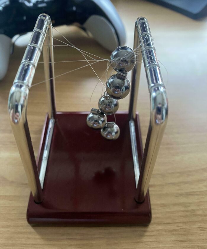 Metallic balls tangled in strings on a Newton’s cradle demonstrating sibling shenanigans and playful chaos.