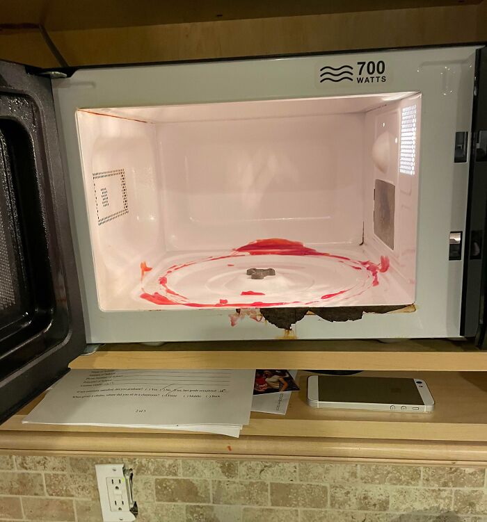 Microwave with red food stains inside and damage on the door, showing sibling shenanigans gone wrong.