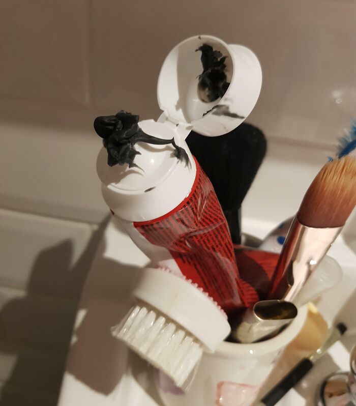 Tube of black paint squeezed messily from the cap, placed in a cup with makeup brushes, sibling shenanigans captured.