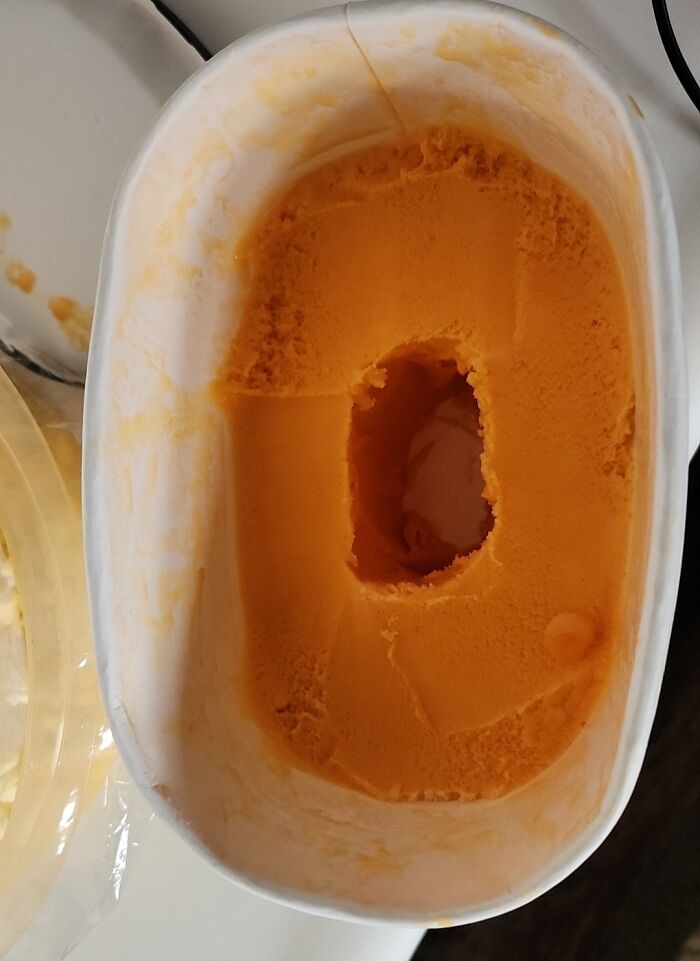 Half-eaten container of orange ice cream showing a rectangular hole in the middle from sibling shenanigans.