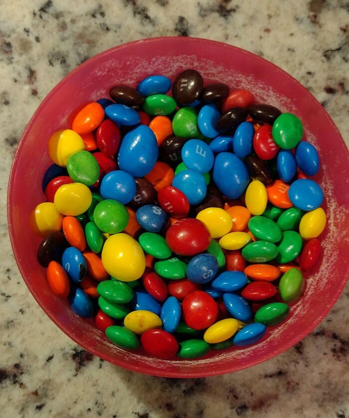 Colorful candy pieces in a red bowl on a speckled countertop, illustrating sibling shenanigans with treats.