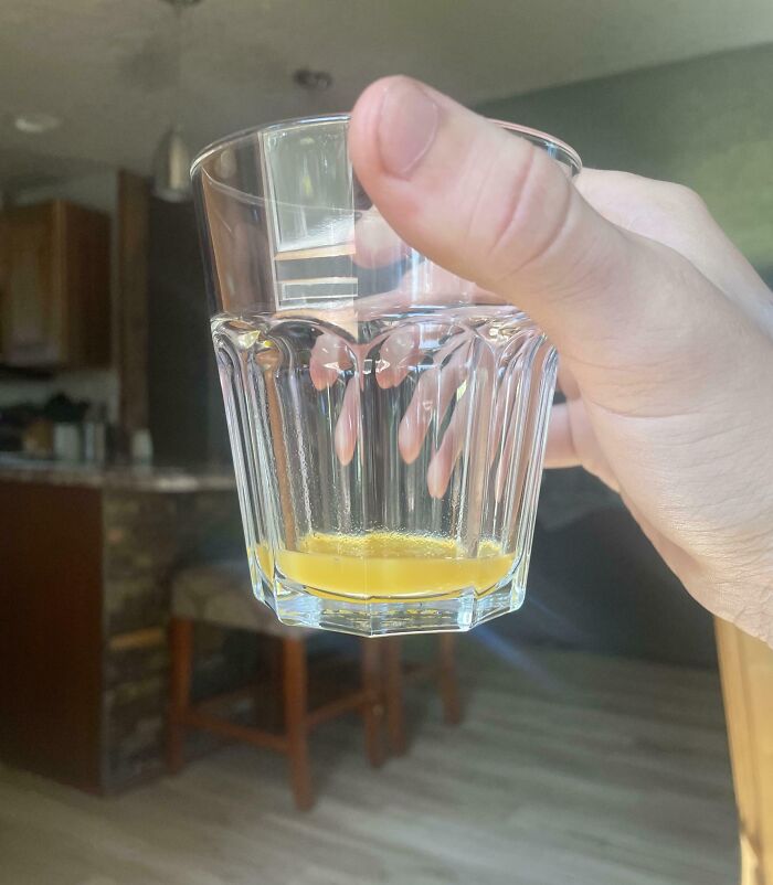 Hand holding a nearly empty glass with a small amount of orange liquid inside, sibling shenanigans concept.