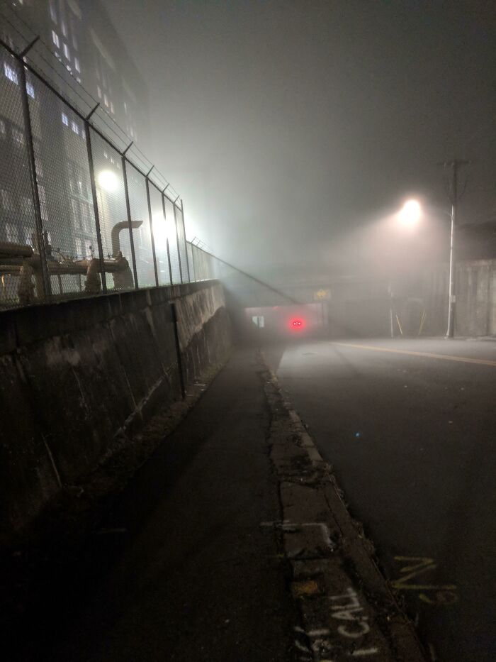 Foggy dimly lit street with two red lights resembling eyes, creating a creepy and unsettling captured moment at night.