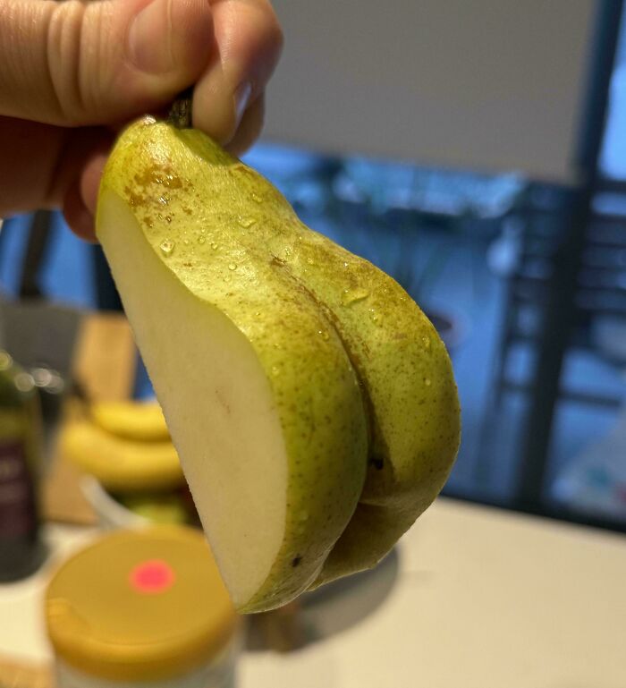 Hand holding a pear cut in half, showing a witty visual resembling a pair of buttocks.