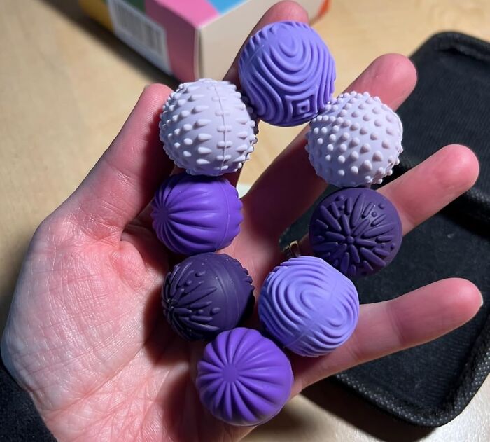Hand holding a set of textured purple and white balls, a popular impulse buy worth the financial decision.