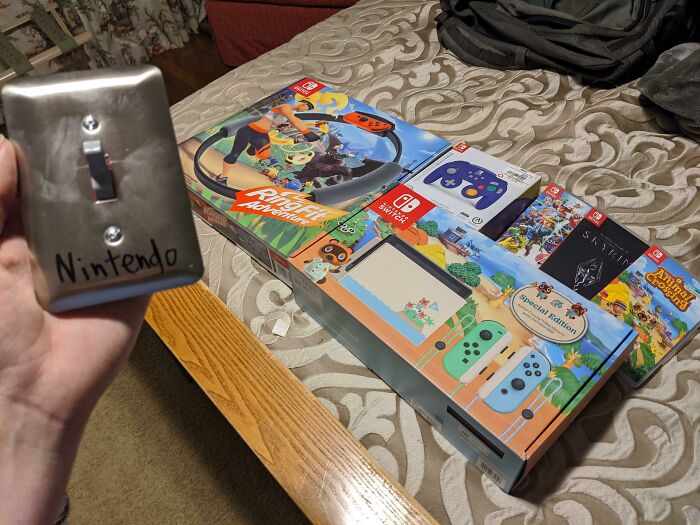 Hand holding a light switch labeled Nintendo next to a Nintendo Switch console and game boxes on a bed, showcasing witty humor.