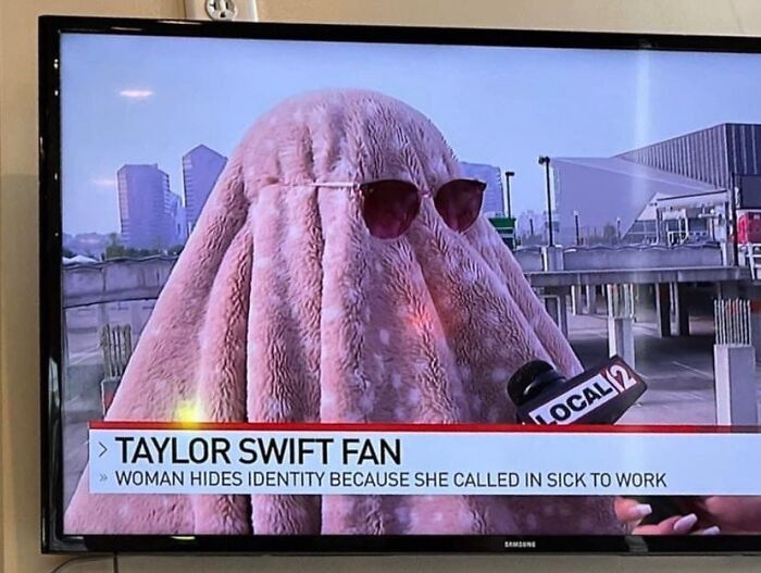 Person covered by a pink blanket and sunglasses being interviewed, showcasing witty humor in a news segment.