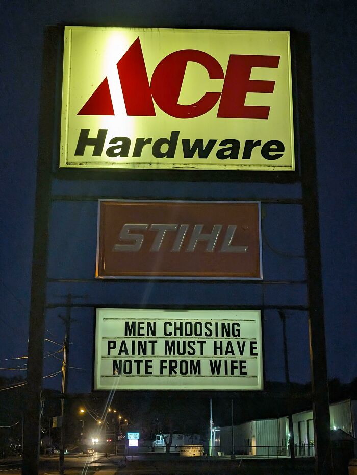 Ace Hardware sign at night with witty message requiring men to have a note from their wife before choosing paint.