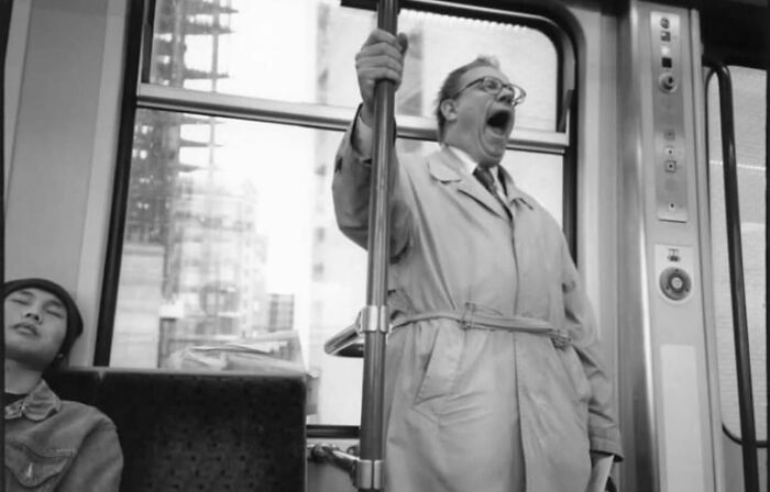 Middle-aged man in trench coat yawning while standing on a crowded subway, a powerful street photo capturing everyday life.