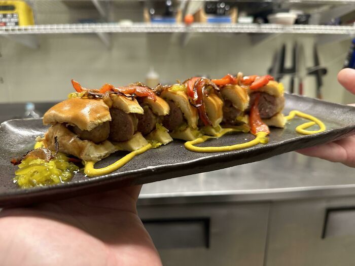 Creative food presentation on a black plate with mustard, roasted peppers, and a witty culinary twist.