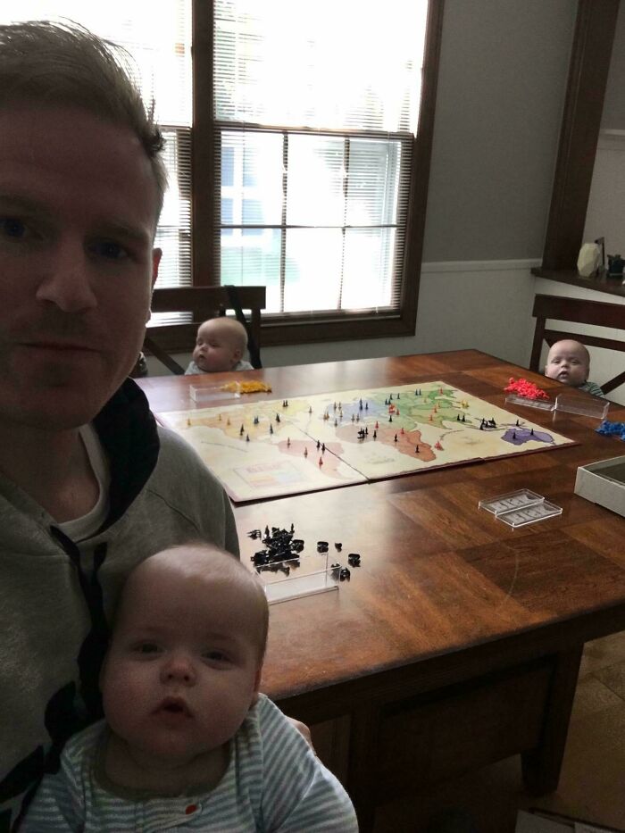 Man playing board game with three babies seated around table, showcasing witty moments captured in everyday life.