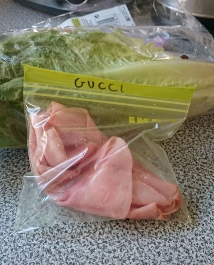 Plastic bag of deli meat labeled Gucci next to lettuce on a kitchen counter showing witty food labeling.