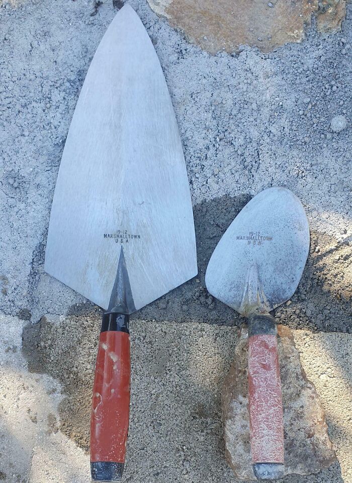 Two different sized gardening trowels side by side on gravel, showing comparisons nobody asked for.