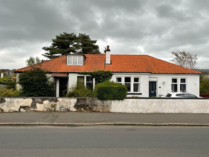 Old white house with orange roof and overgrown bushes on a cloudy day, illustrating comparisons in everyday scenes.
