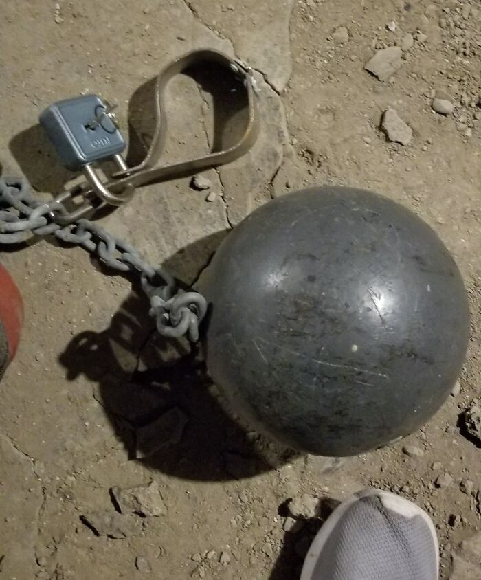 Close-up of a rusty chain and ball with a lock on c*****d dirt ground, creating a creepy and unsettling moment.