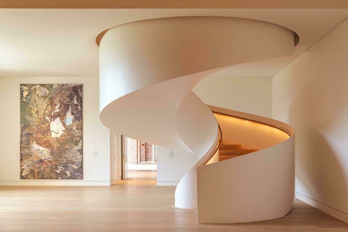 Modern minimalist architecture featuring a graceful, curving white spiral staircase in a sunlit interior.