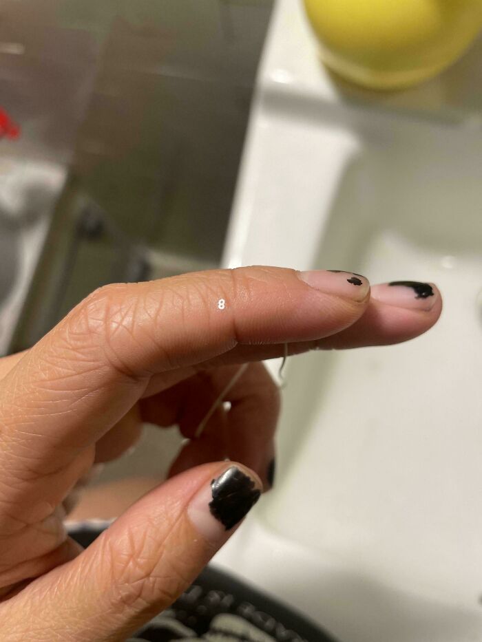 Close-up of a hand with chipped black nail polish holding a thin wire, a moderately interesting everyday moment shared online.
