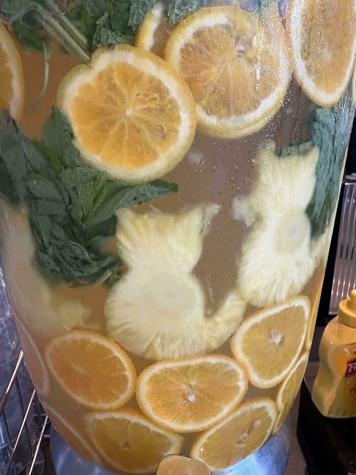 Close-up of a beverage dispenser with lemon slices, mint leaves, and pineapple pieces creating a moderately interesting drink display.