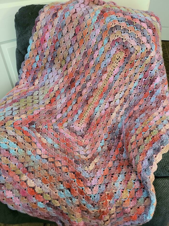 Multicolored crochet blanket with intricate stitch patterns draped over a dark fabric chair showcasing crocheting artistry.