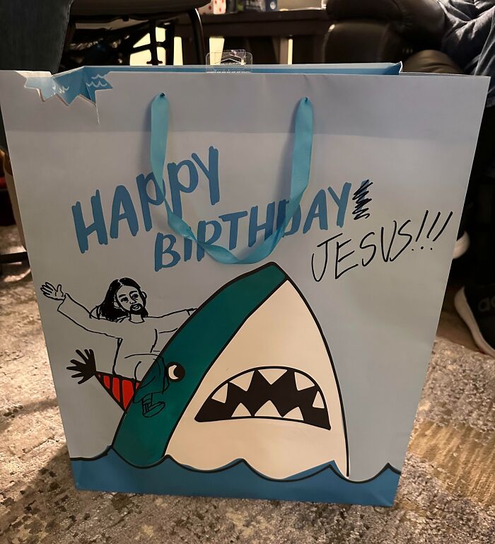 Birthday gift bag with a funny cartoon of Jesus riding a shark and the words happy birthday, showcasing witty humor.