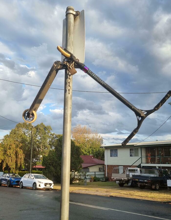 A humorously locked and chained scooter frame hanging on a street sign pole showing witty security.