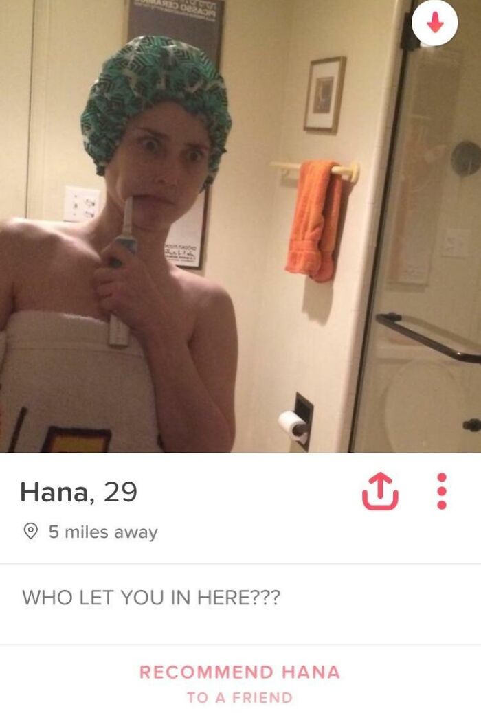 Woman in bathroom with shower cap and towel pretending to brush teeth, showcasing witty humor in a candid selfie.