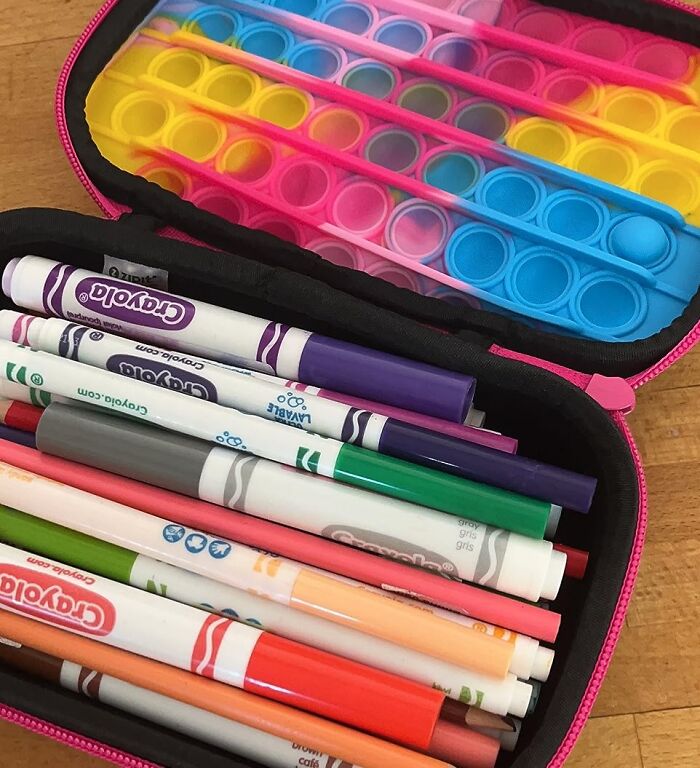 Colorful markers and a rainbow pop-it fidget toy inside a pink pencil case for back to school finds.