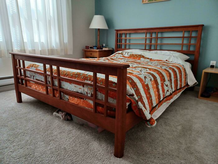 Woodworkers crafted a detailed wooden bed frame in a cozy bedroom with a patterned quilt and natural lighting.