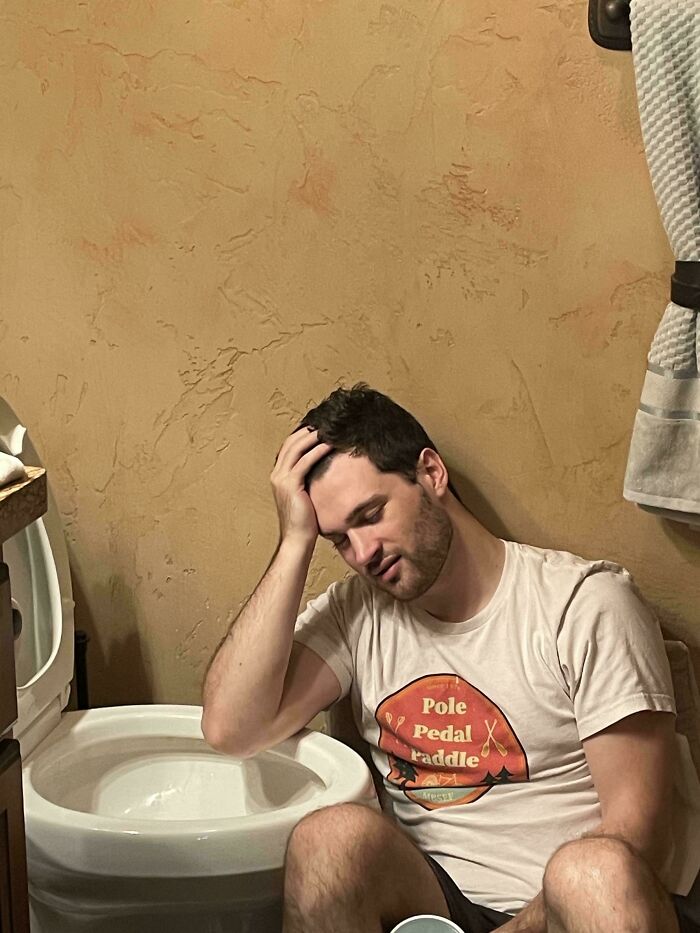 Man sitting on the floor leaning against a textured wall by a toilet, captured in an accidental Renaissance photo style.