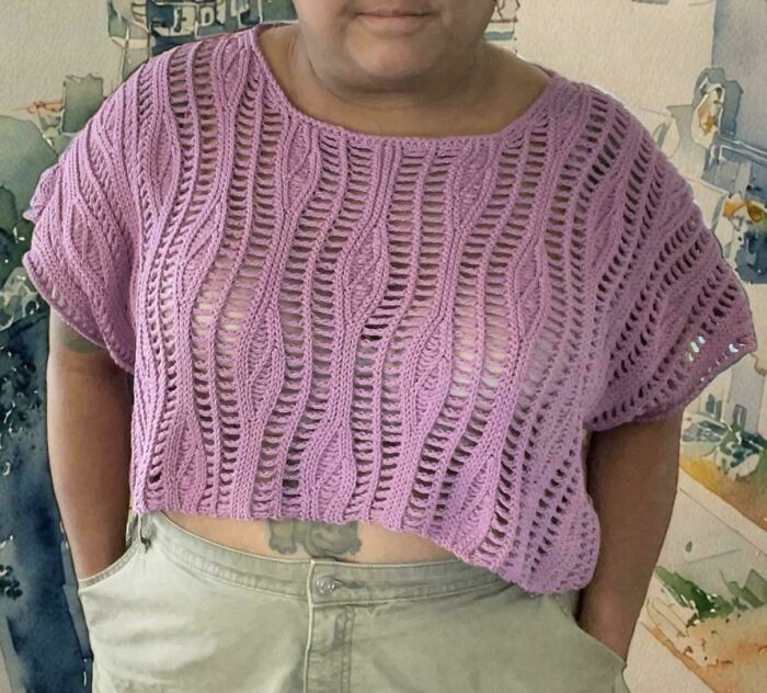 Person wearing a hand-crocheted purple top showcasing detailed stitch patterns in a casual indoor setting.