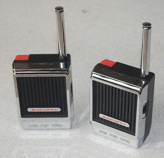 Two vintage Archer walkie-talkies with antennas standing on a light-colored surface, evoking nostalgic feelings.