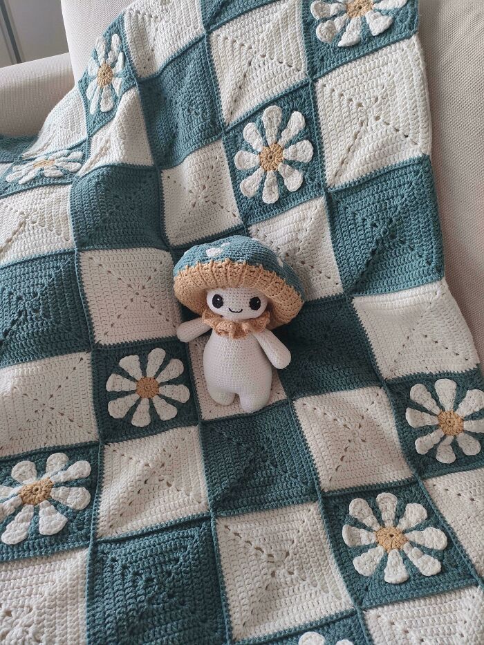 Crocheted blanket with daisy patterns and a handmade mushroom doll showcasing expert crocheting skills.
