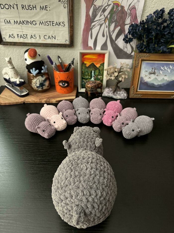 Crocheted hippo family in various colors displayed on a black table with artistic decor in the background.
