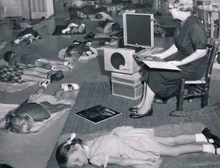 Children taking a nap on the floor while a woman reads a book next to an old television, evoking feel old nostalgia.