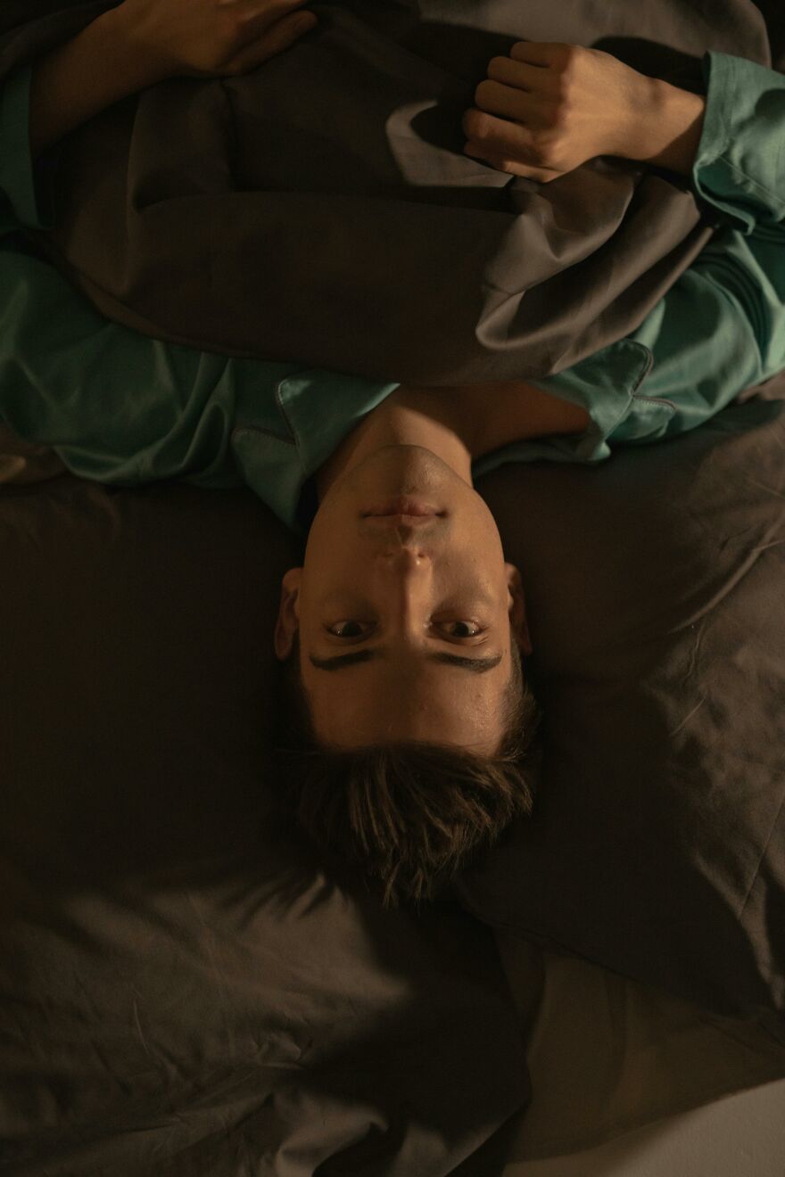Young man lying awake in bed at night, showing signs soul ties still grip with a troubled expression.