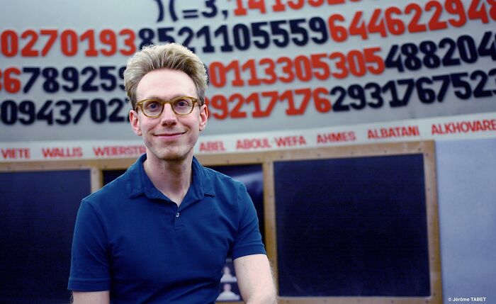 Man with glasses and blond hair smiling in front of a colorful numerical display showcasing superhuman abilities.