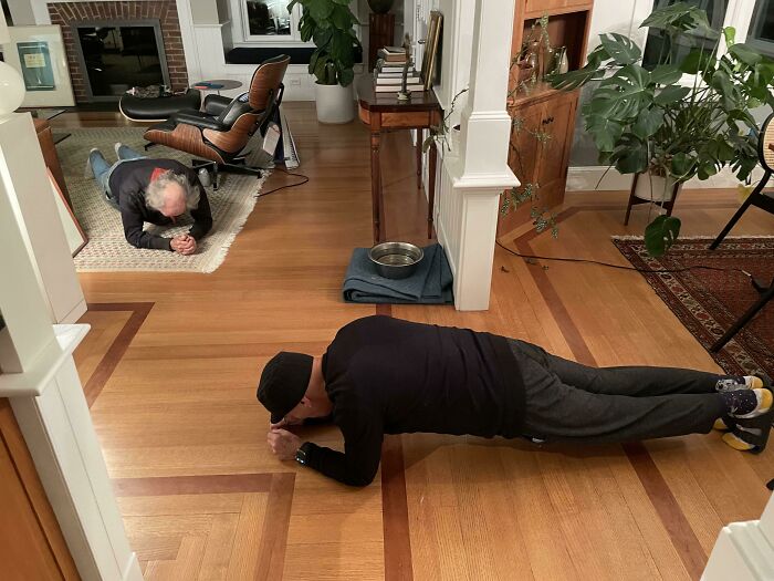 Two wholesome kind neighbors exercising together indoors on hardwood floors in a cozy living room setting.